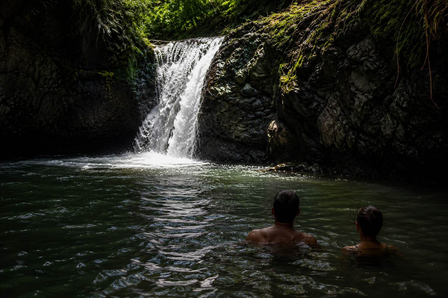 A couple swimming in a serene jungle pool beneath a waterfall near Casa Venado