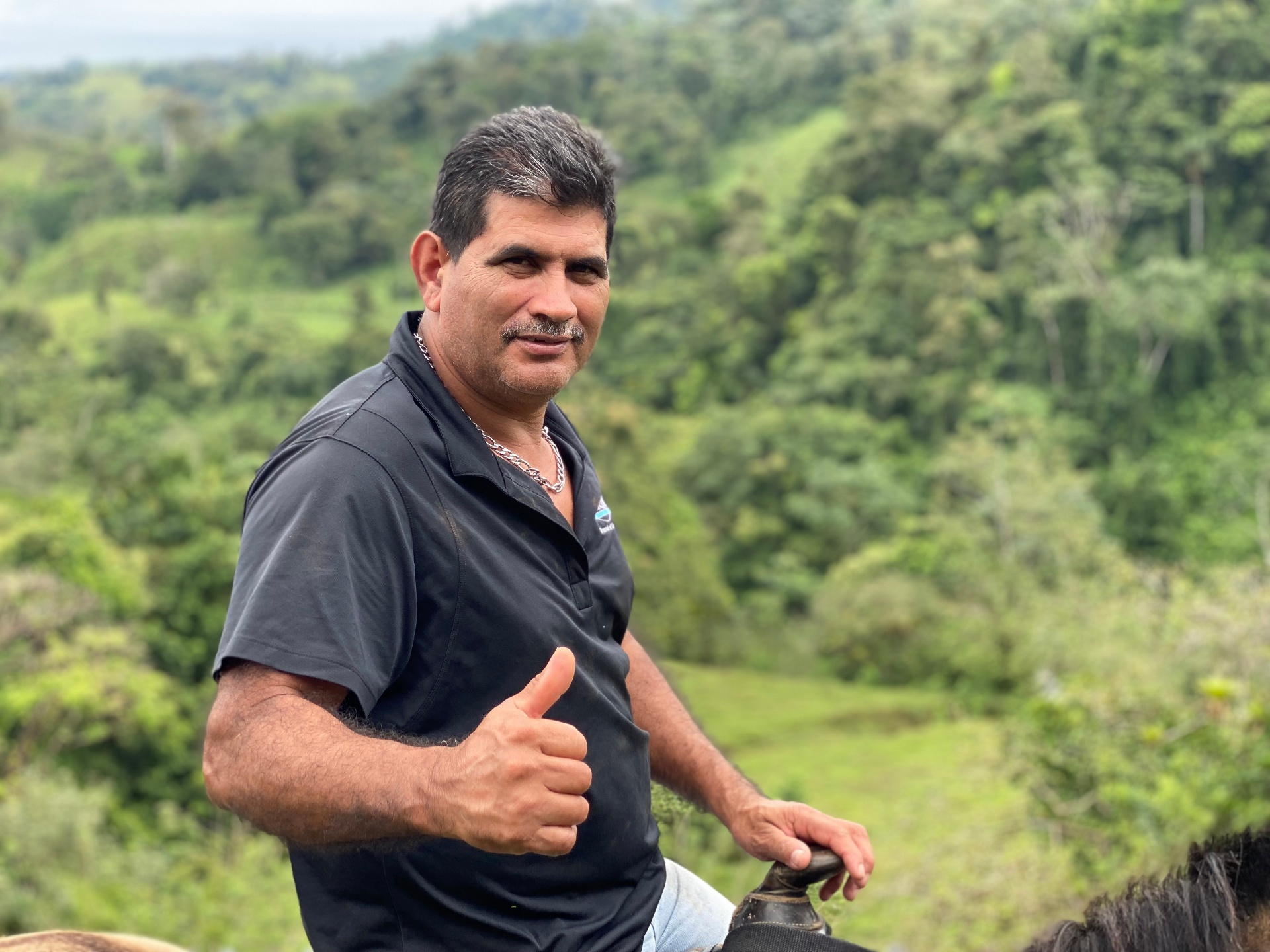 Ronal on horseback giving a thumbs up with the green Venado hills behind him